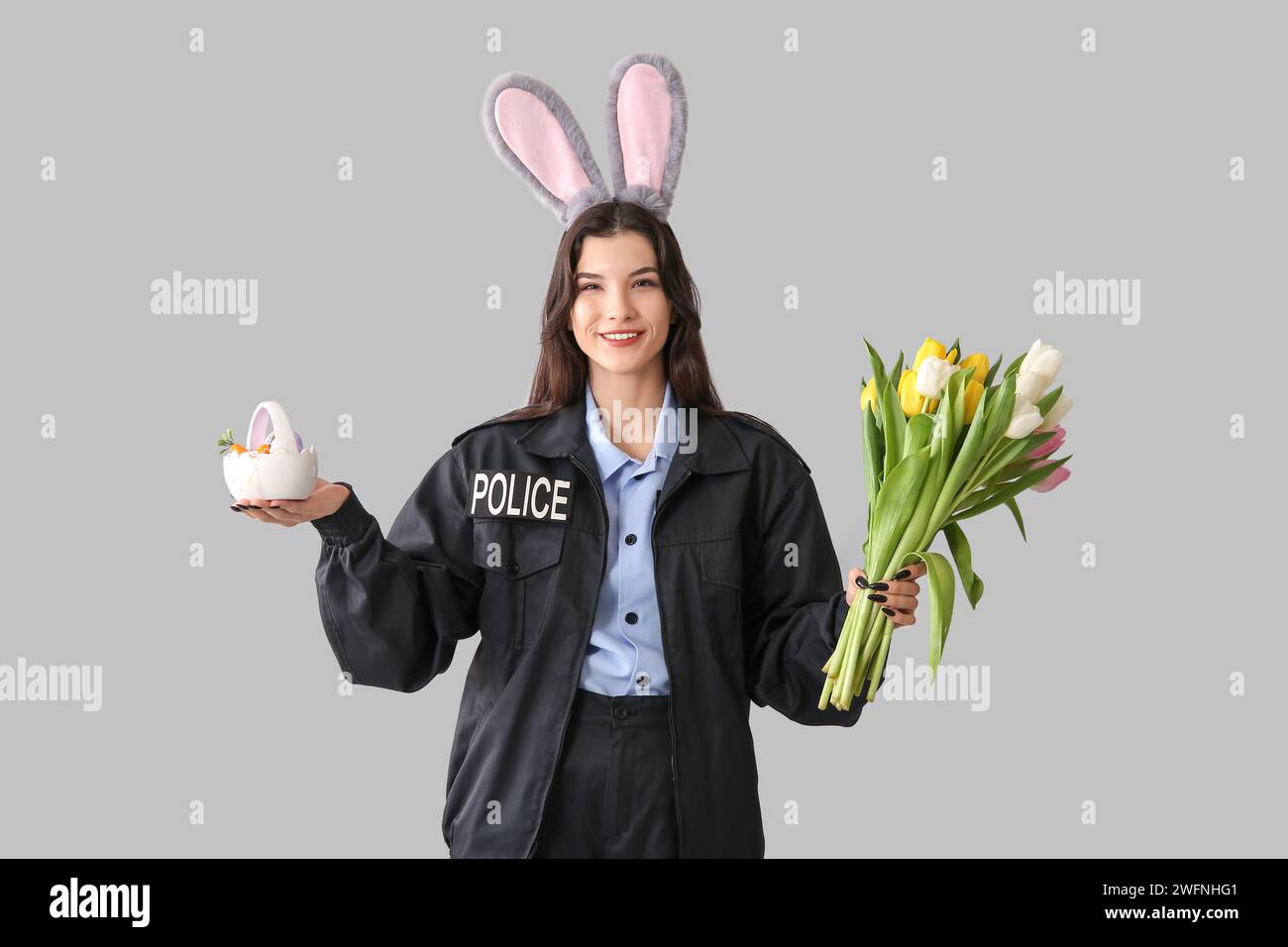 Agente di polizia donna in orecchie conigliate con uova di Pasqua e tulipani su sfondo chiaro Foto Stock