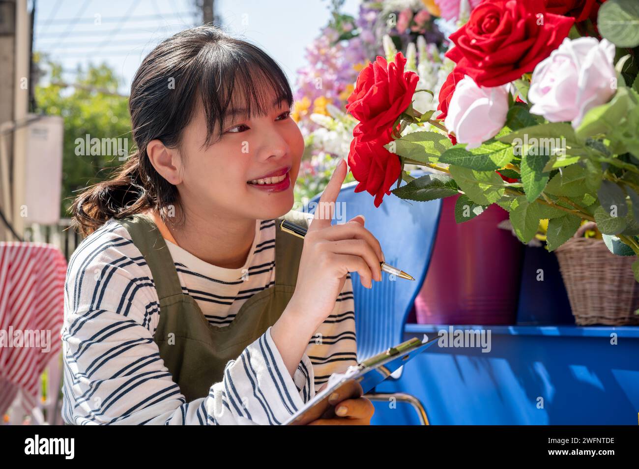 Una giovane e felice lavoratrice asiatica lavora nel giardino del suo negozio per controllare le scorte di fiori. una piccola impresa, imprenditore Foto Stock