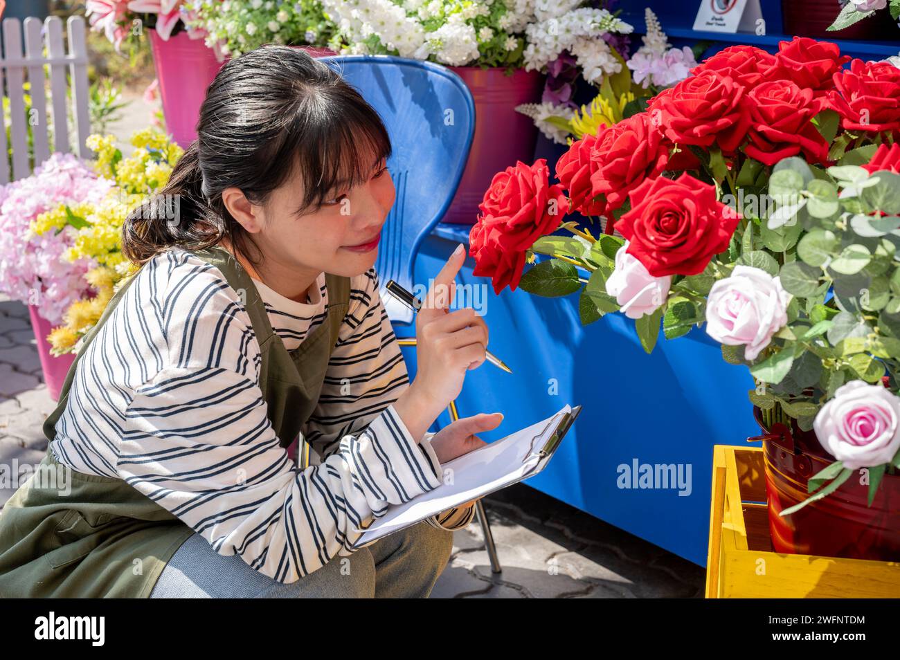 Una giovane e felice lavoratrice asiatica lavora nel giardino del suo negozio per controllare le scorte di fiori. una piccola impresa, imprenditore Foto Stock