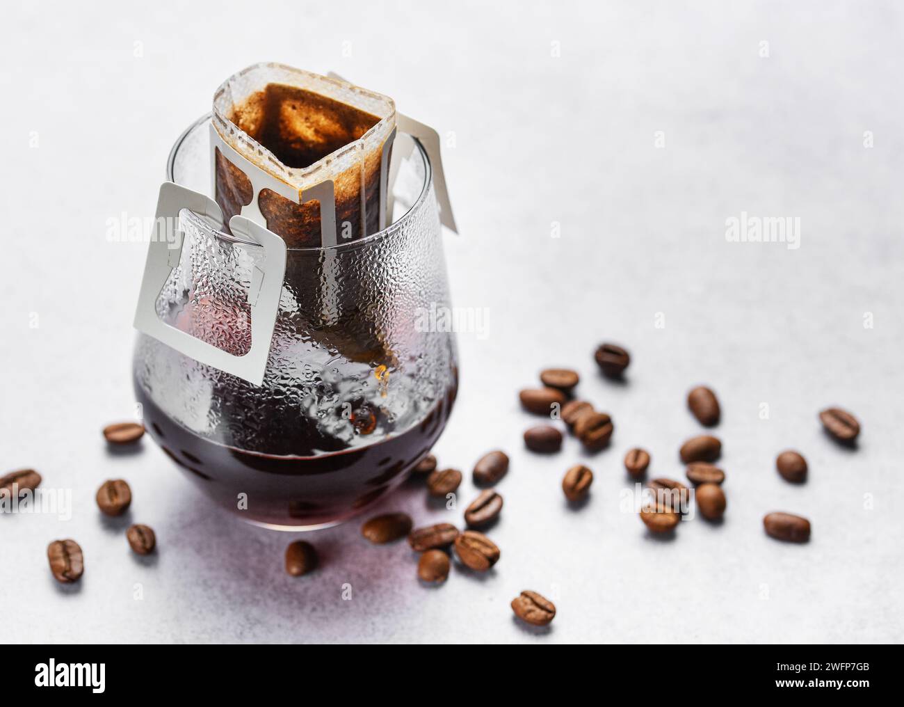 Un bicchiere di caffè gocciolante appena fatto. Versare il sacchetto del caffè con il caffè macinato per l'erogazione in un bicchiere Foto Stock