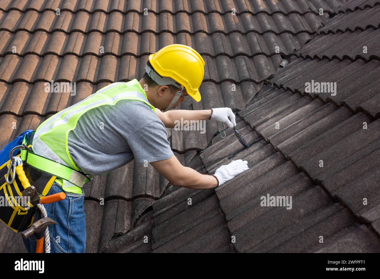 Lavoratore che utilizza una riparazione impermeabile del rivestimento del tetto per riparare le crepe del vecchio tetto in tegole. Foto Stock