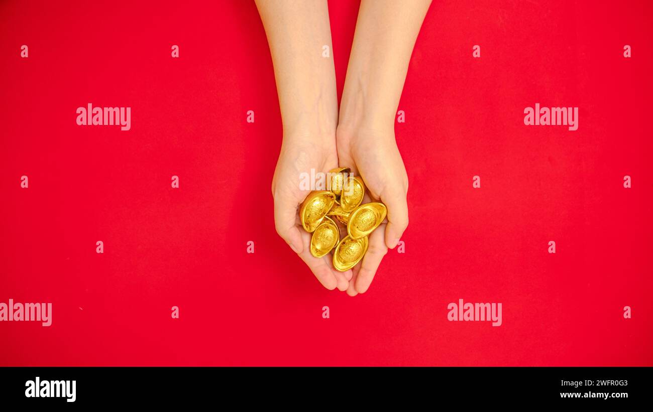 Un piatto di mano che regge un sacco di lingotto d'oro cinese dall'alto per festeggiare il Capodanno lunare cinese, tema rosso Foto Stock
