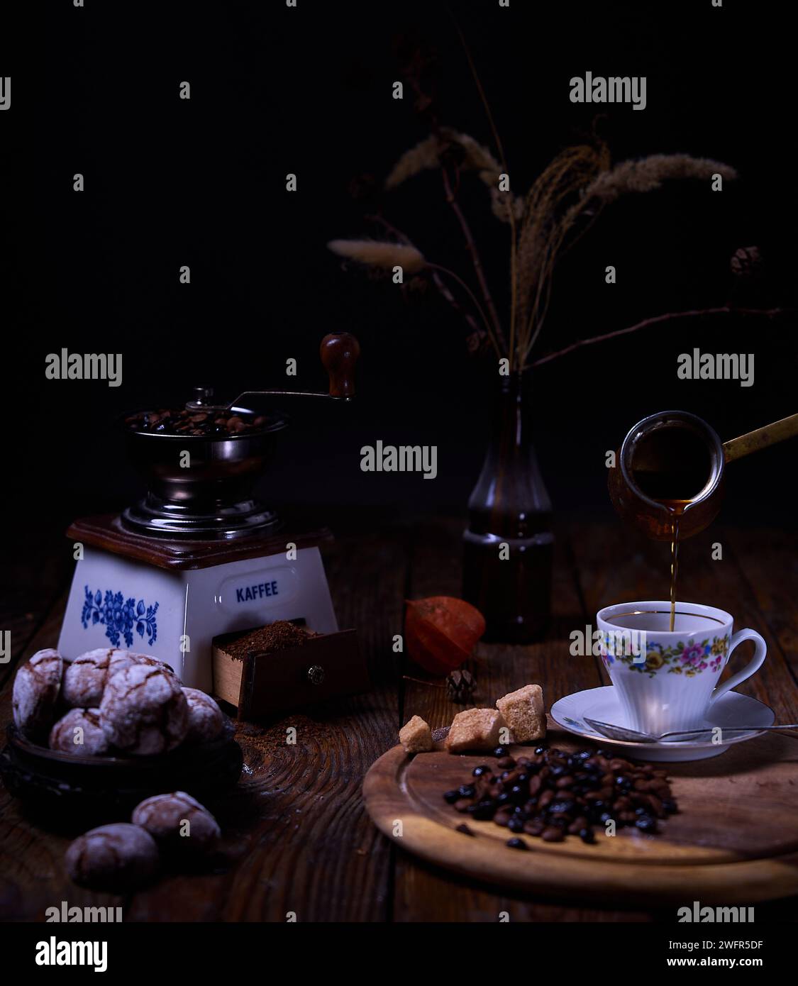 Composizione del caffè. Il caffè viene versato da una tazza turca in una tazza, un macinacaffè, caffè macinato e chicchi di caffè, biscotti croccanti al cioccolato e secchi Foto Stock