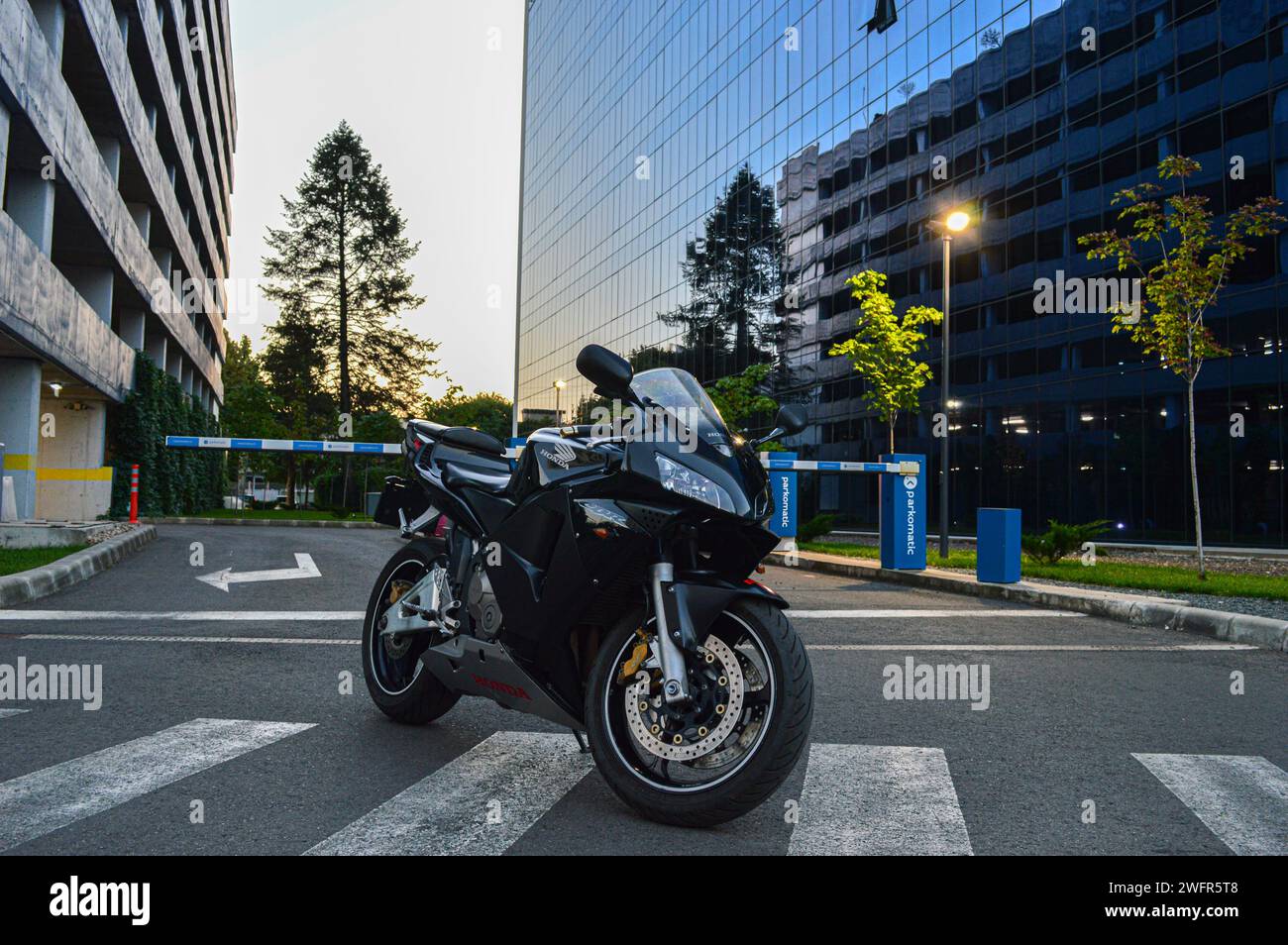Una motocicletta parcheggiata in una strada vicino a un edificio al tramonto. Foto Stock