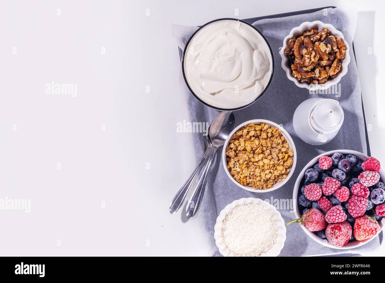 Preparazione della cottura con sfondo di corteccia di yogurt congelato con yogurt greco, bacche fresche, muesli, miele, salsa al cioccolato, con vassoio da forno deco. Vista dall'alto della donna Foto Stock