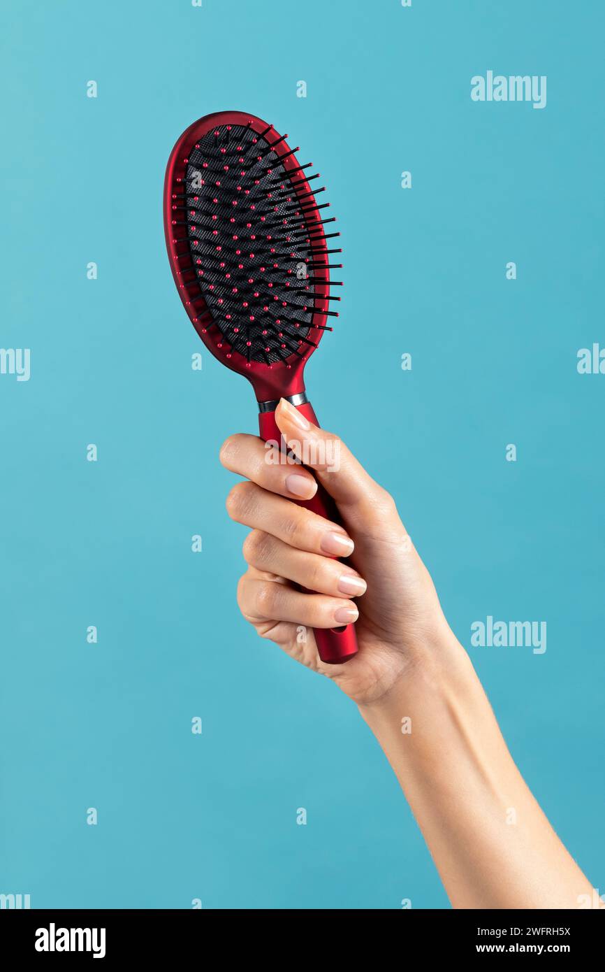 Ritaglia la mano femminile anonima tenendola in mano e mostrando in studio una pratica spazzola per capelli con setole in plastica su sfondo blu Foto Stock