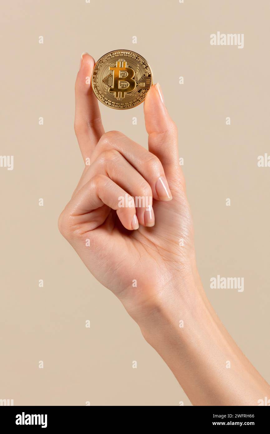 Crop Anonymous Female che manifesta bitcoin dorati su sfondo beige in criptovaluta leggera, scambio elettronico e profi finanziari Foto Stock