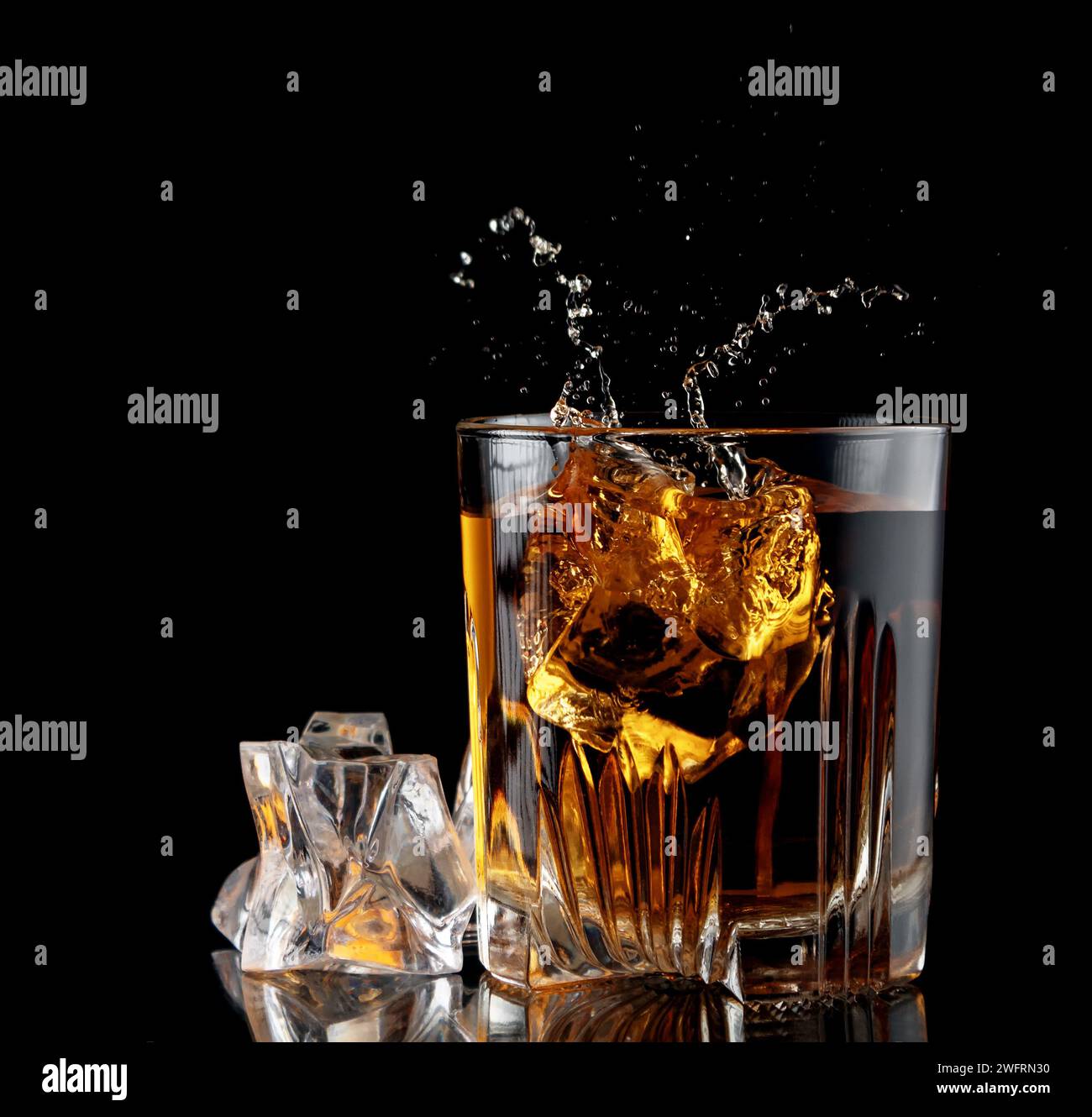Bicchiere con whisky e cubetto di ghiaccio cadente con schizzi su sfondo nero. Foto Stock