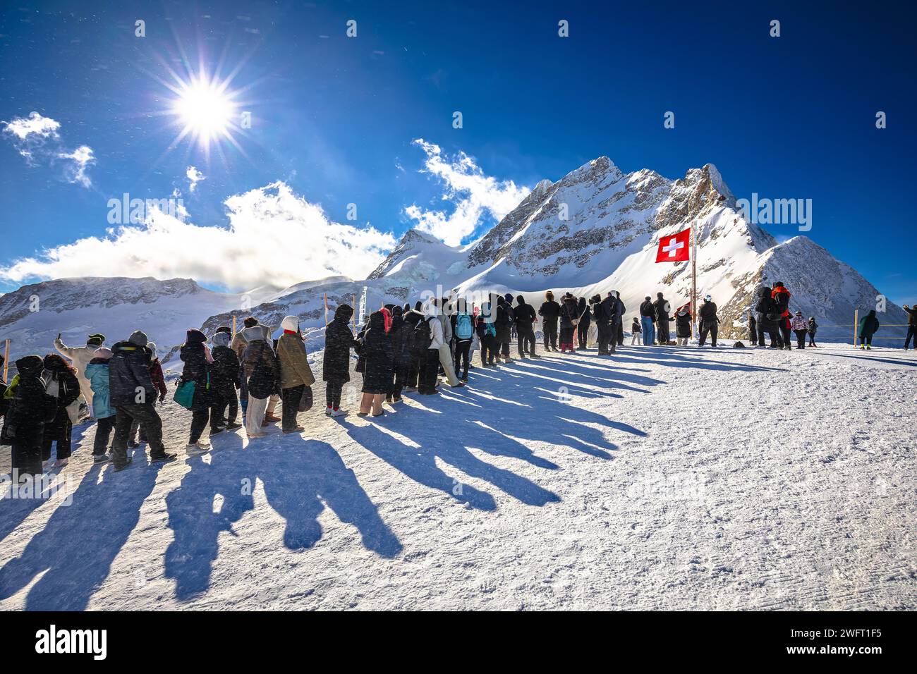 I turisti in fila per scattare una foto di fronte alla bandiera svizzera sul picco dello Jungfraujoch, regione svizzera dell'Oberland Berner Foto Stock