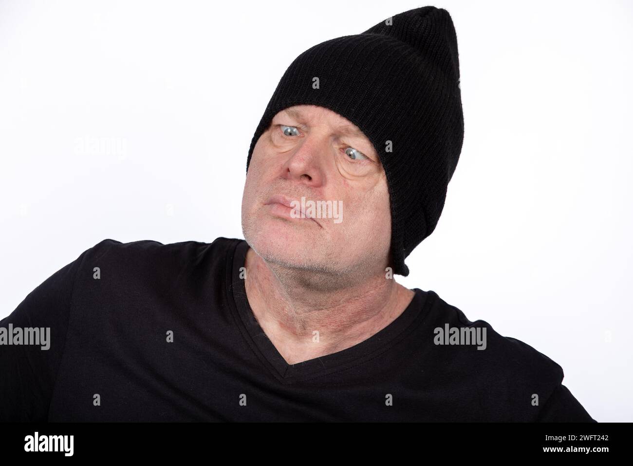 Eccentrico uomo di mezza età con T-shirt e cappello nero con espressione a croce, personaggio umoristico su sfondo bianco - concetto di Ritratto eccentrico Foto Stock