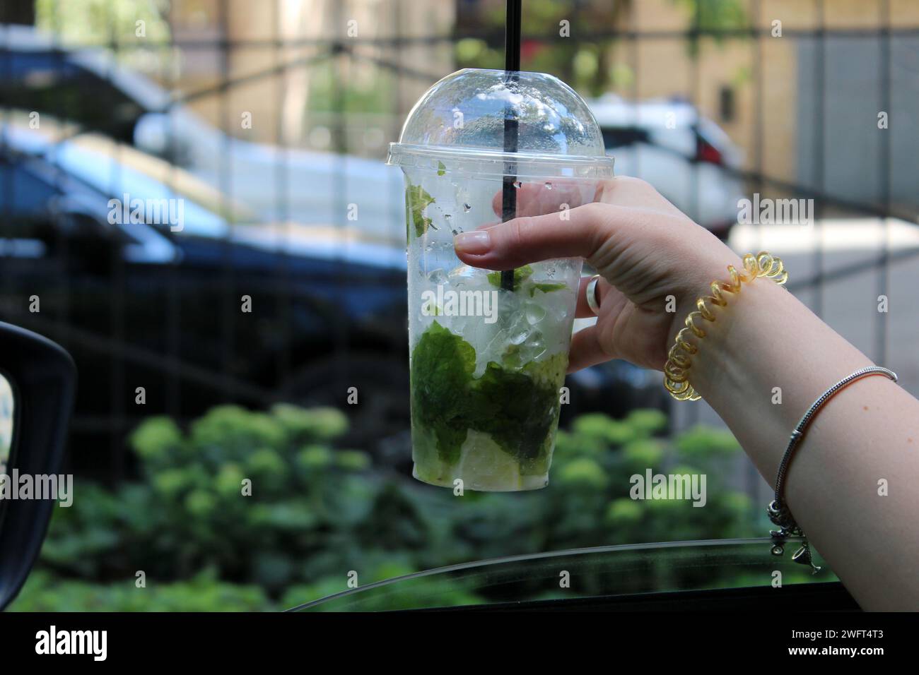 Mano di donna con un cocktail alcolico sulla porta di una macchina con un vetro arrotolato Foto Stock