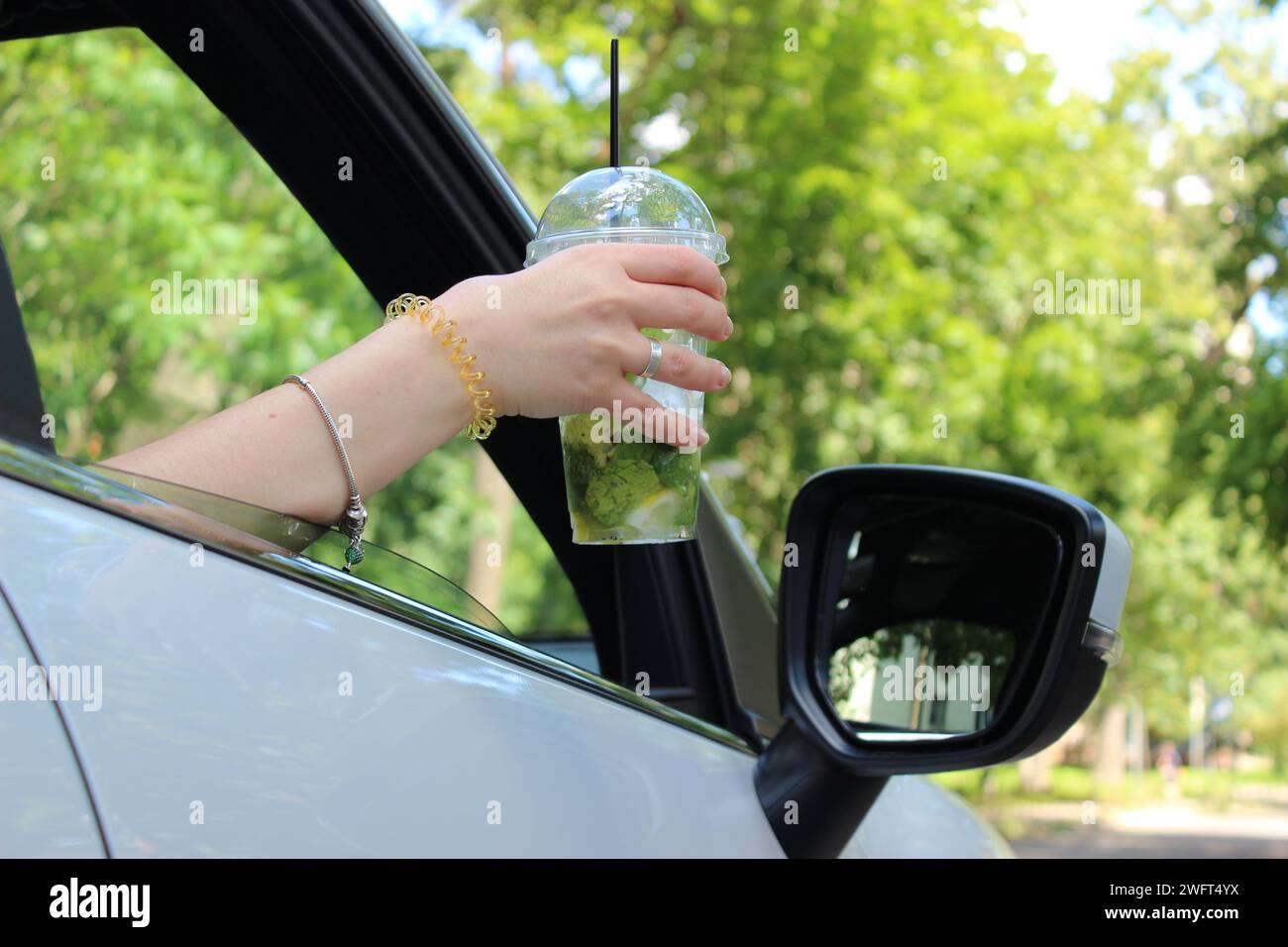 Vista dal basso di un cocktail alcolico nella mano di una donna sul sedile del passeggero di un'auto Foto Stock