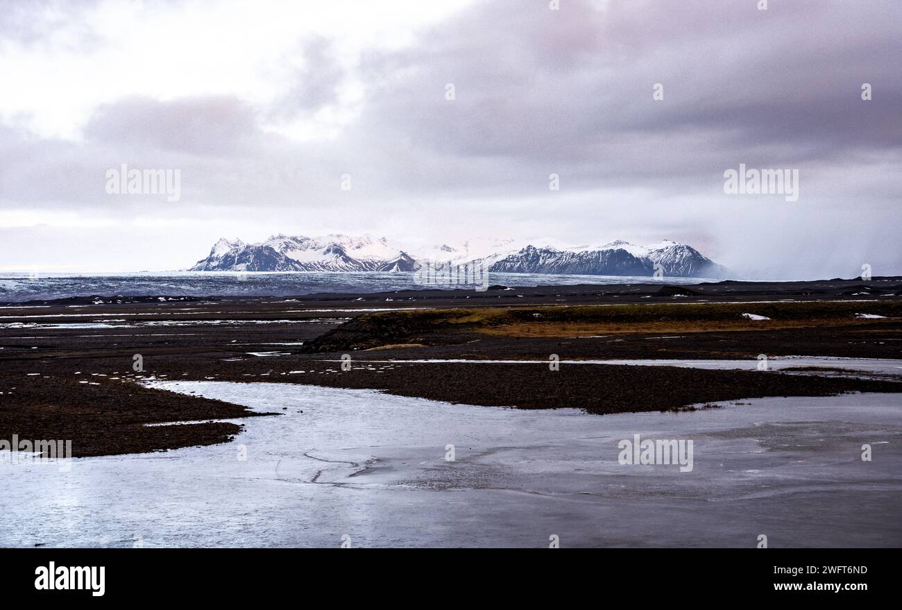 Un fiume sereno che scorre su un terreno roccioso con maestose montagne innevate sullo sfondo Foto Stock