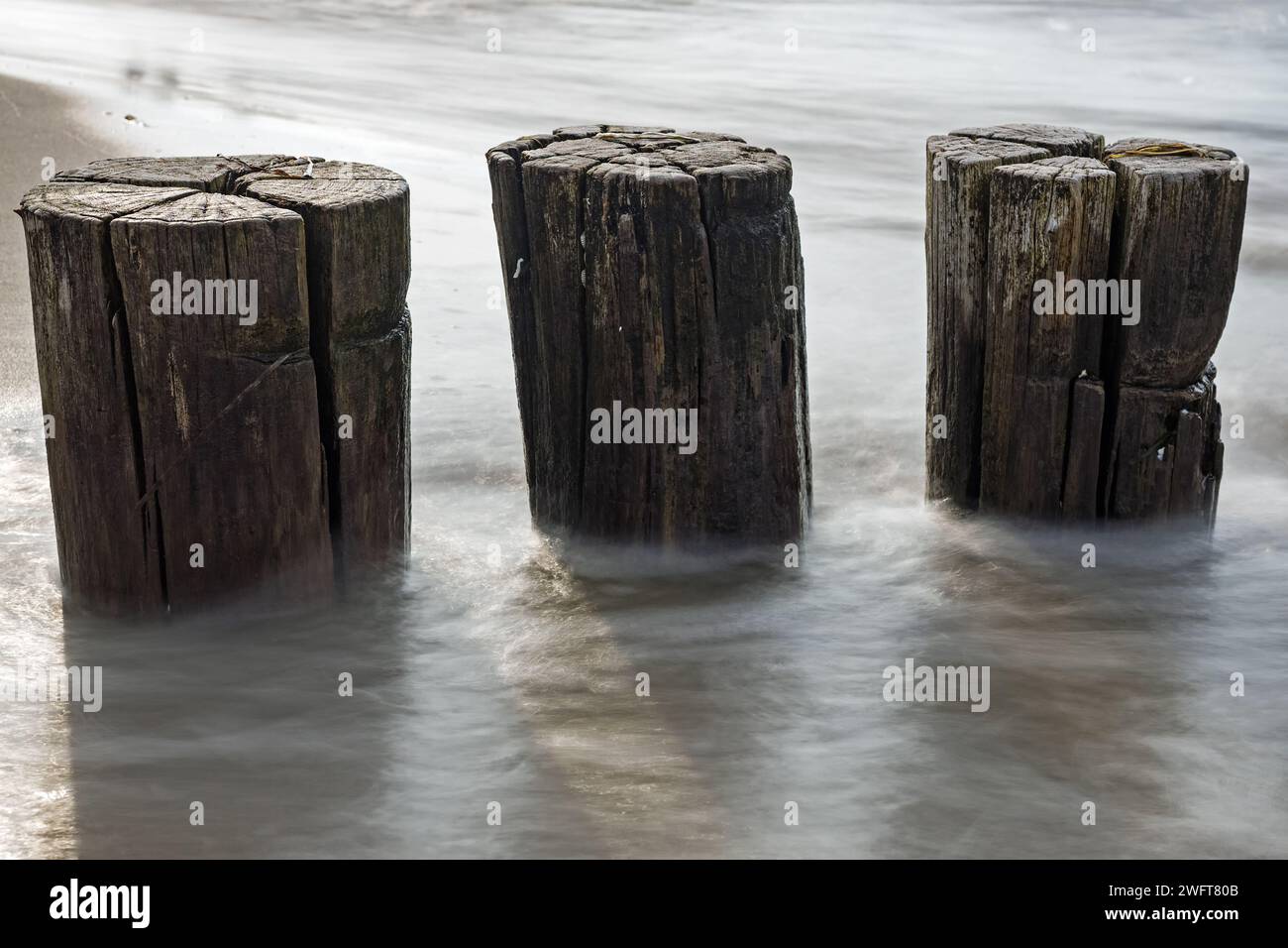 Primo piano di tre groynes di legno nel Mar Baltico con lunga esposizione Foto Stock