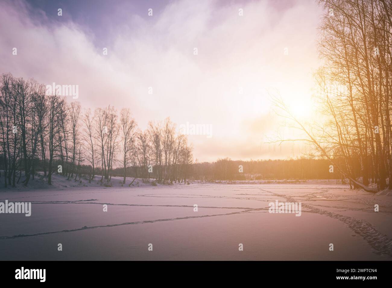 Tramonto o alba su uno stagno ghiacciato con betulle lungo le rive in inverno. Estetica vintage. Foto Stock