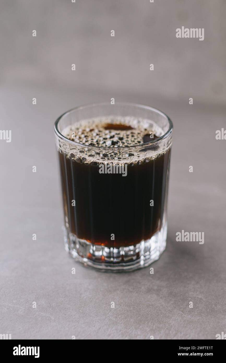 Caffè gocciolante appena fatto in una tazza di vetro. Una tazza di caffè su sfondo grigio. Foto Stock