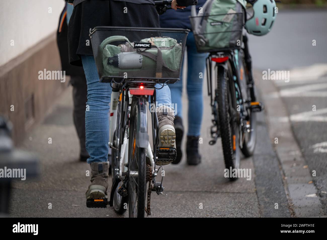 , Alltagssituation, Deutschland, 01.02.2024, Zwei Personen gehen auf einem Gehweg, eine davon schiebt ein Fahrrad mit einem Korb und einem Helm auf d Foto Stock