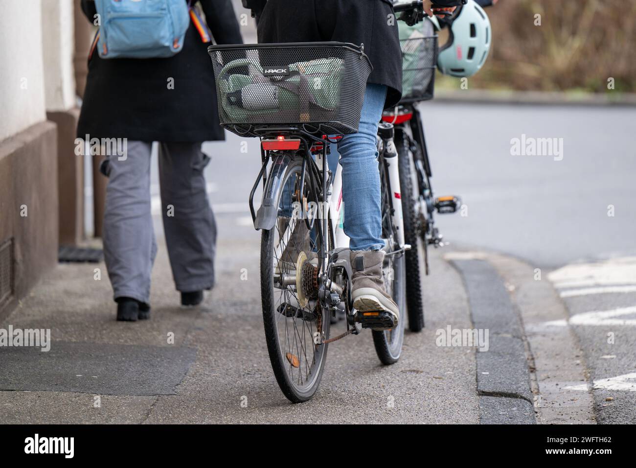 , Alltagssituation, Deutschland, 01.02.2024, Zwei Personen gehen auf einem Gehweg, eine davon schiebt ein Fahrrad mit einem Korb und einem Helm auf d Foto Stock