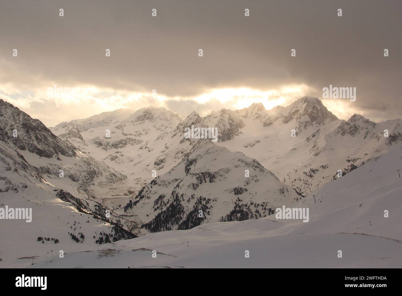 I caldi raggi del sole che spuntano attraverso le nuvole invernali. Montagne alpine. Foto Stock