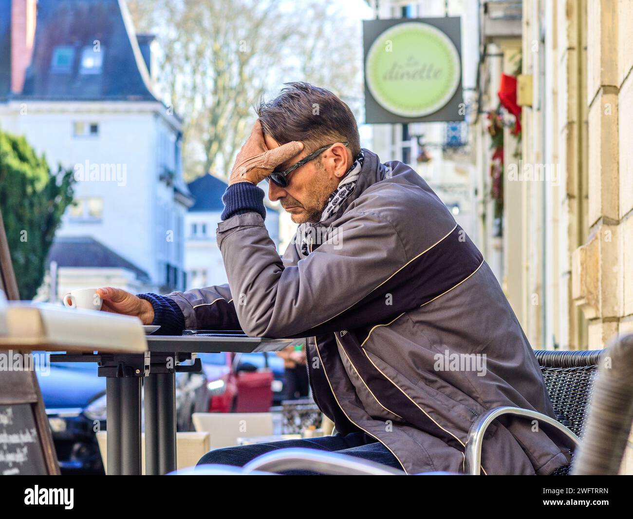 Uomo pensivo sedeva a un tavolo da caffè all'aperto usando uno smartphone - Tours, Indre-et-Loire (37), Francia. Foto Stock