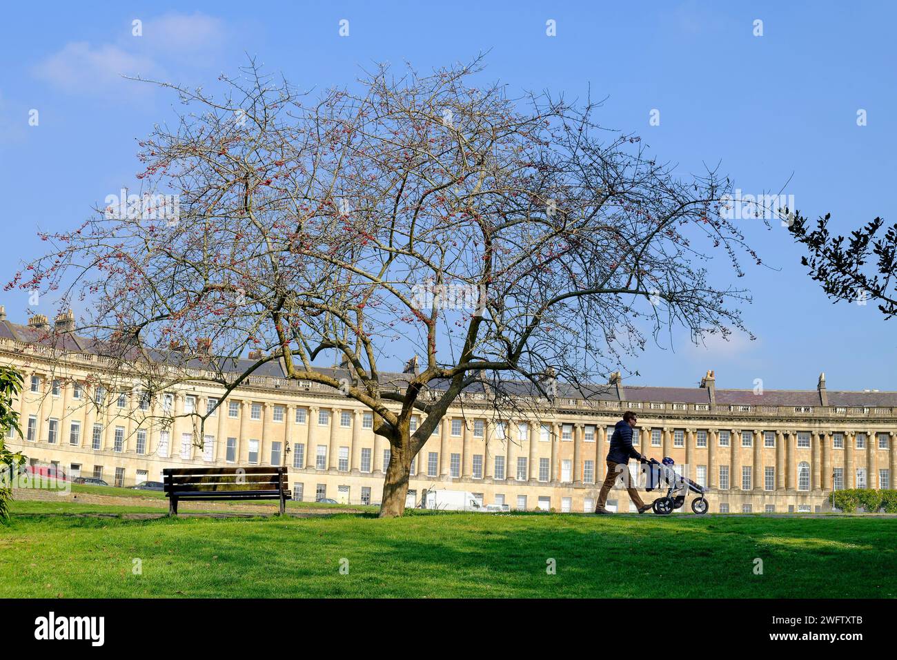 In un giorno di primavera di sole, un uomo viene ritratto spingendo un passeggino davanti al famoso Royal Crescent di Bath, Somerset, Inghilterra, Regno Unito. Foto Stock