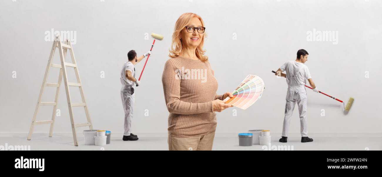 Donna con una tavolozza di colori e pittrice che dipinge un muro dietro Foto Stock