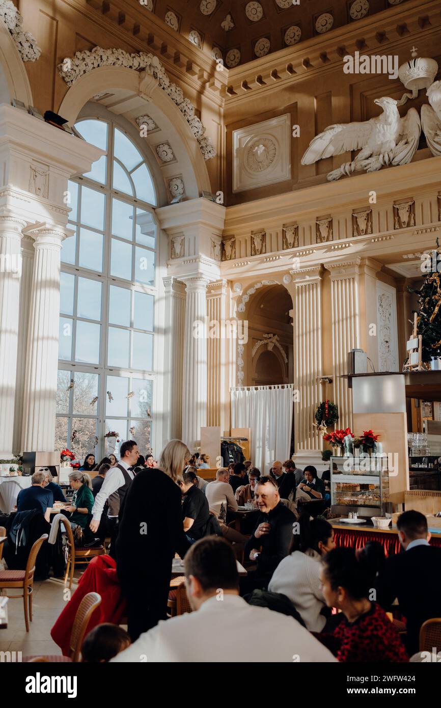 Gruppo di persone sedute ai tavoli all'interno di un edificio riccamente decorato, che vanta ampie finestre Foto Stock