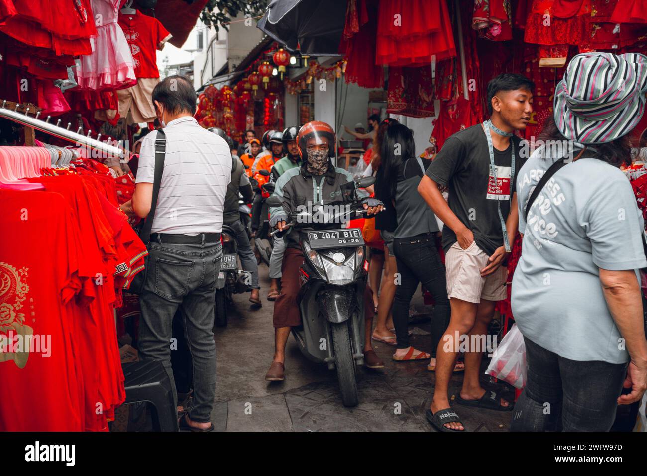 Uomini in bicicletta in una stretta strada del mercato tradizionale con gente in giro Foto Stock