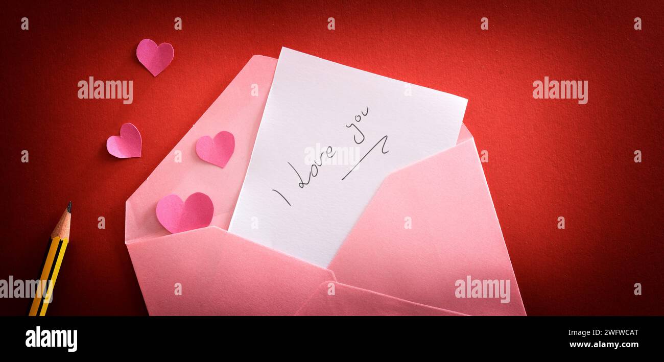 Nota d'amore con messaggio ti amo in una busta rosa su sfondo rosso sfumato con cuori e matita rosa. Vista dall'alto. Foto Stock
