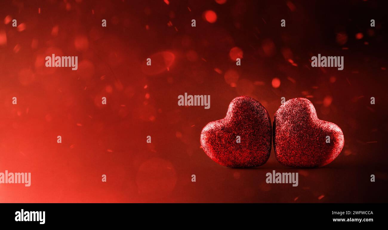 Sfondo due cuori di glitter rossi su sfondo rosso sfumato con particelle volanti. Vista frontale. Foto Stock