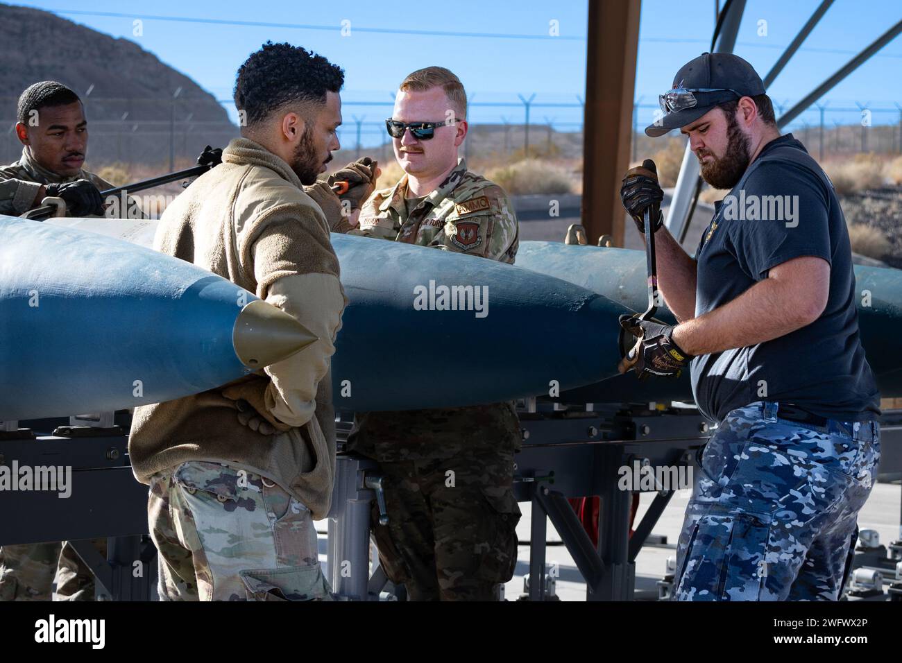 Tre avieri dell'aeronautica statunitense del 57th Munitions Squadron presso la Nellis Air Force base (AFB) e il 31st Munitions Squadron ad Aviano AFB lavorano al fianco del dirigente della Royal Australian Air Force Marcus Blair, a destra, per installare tappi nasali su una bomba da addestramento inerte a Nellis AFB, Nevada, 18 gennaio, 2024. Red Flag-Nellis è un'esercitazione di addestramento al combattimento e fornisce opportunità alla U.S. Air Force e ai suoi alleati di addestrarsi e lavorare insieme per raggiungere obiettivi simili. (Questa foto è stata alterata per motivi di sicurezza sfocando il badge di identificazione) Foto Stock