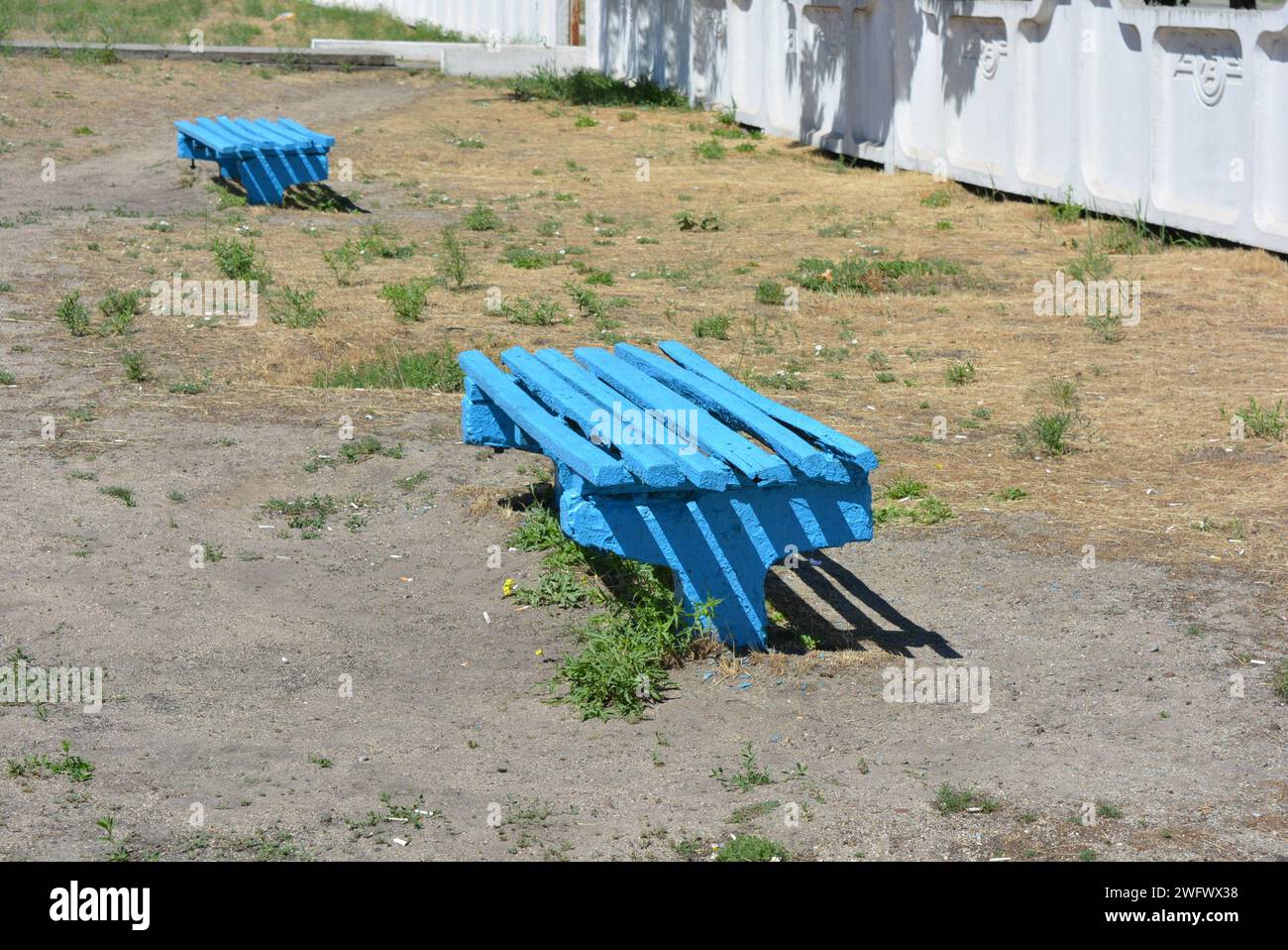 Le solite panchine in legno sono dipinte di blu e si trovano non lontano dalla fermata ferroviaria. Foto Stock