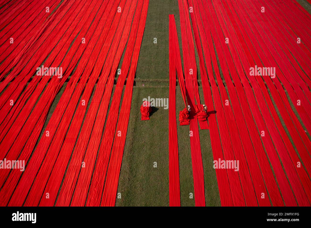 Vista aerea di centinaia di metri di cotone rosso brillante appena tinto si estendono per asciugare al sole a Narsingdi, Bangladesh. Foto Stock
