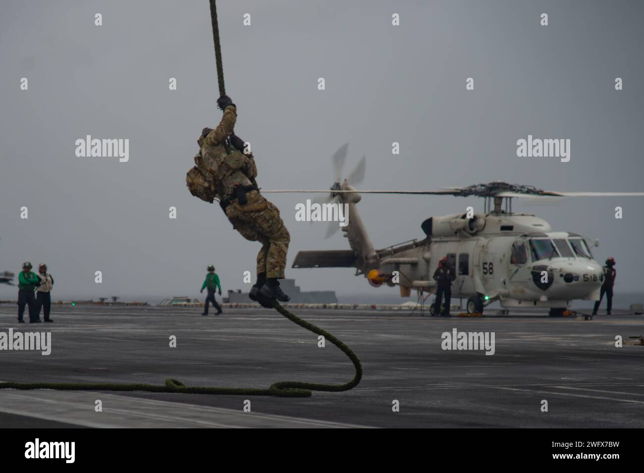 240118-N-PQ495-1265 SOUTH CHINA SEA (18 gennaio 2024) Un operatore Naval Special Warfare (NSW) respinge un MH-60S Sea Hawk, assegnato ai "Black Knights" dell'Helicopter Sea Combat Squadron (HSC) 4, durante un'evoluzione rapida della corda sul ponte di volo della portaerei classe Nimitz USS Carl Vinson (CVN 70). La Vinson, ammiraglia del Carrier Strike Group ONE, è dispiegata nell'area operativa della settima flotta degli Stati Uniti a sostegno di una Indo-Pacifico libera e aperta. Naval Special Warfare è la forza operativa marittima d'élite degli Stati Uniti, in posizione unica per estendere la portata della flotta e ottenere e mantenere la conformità Foto Stock