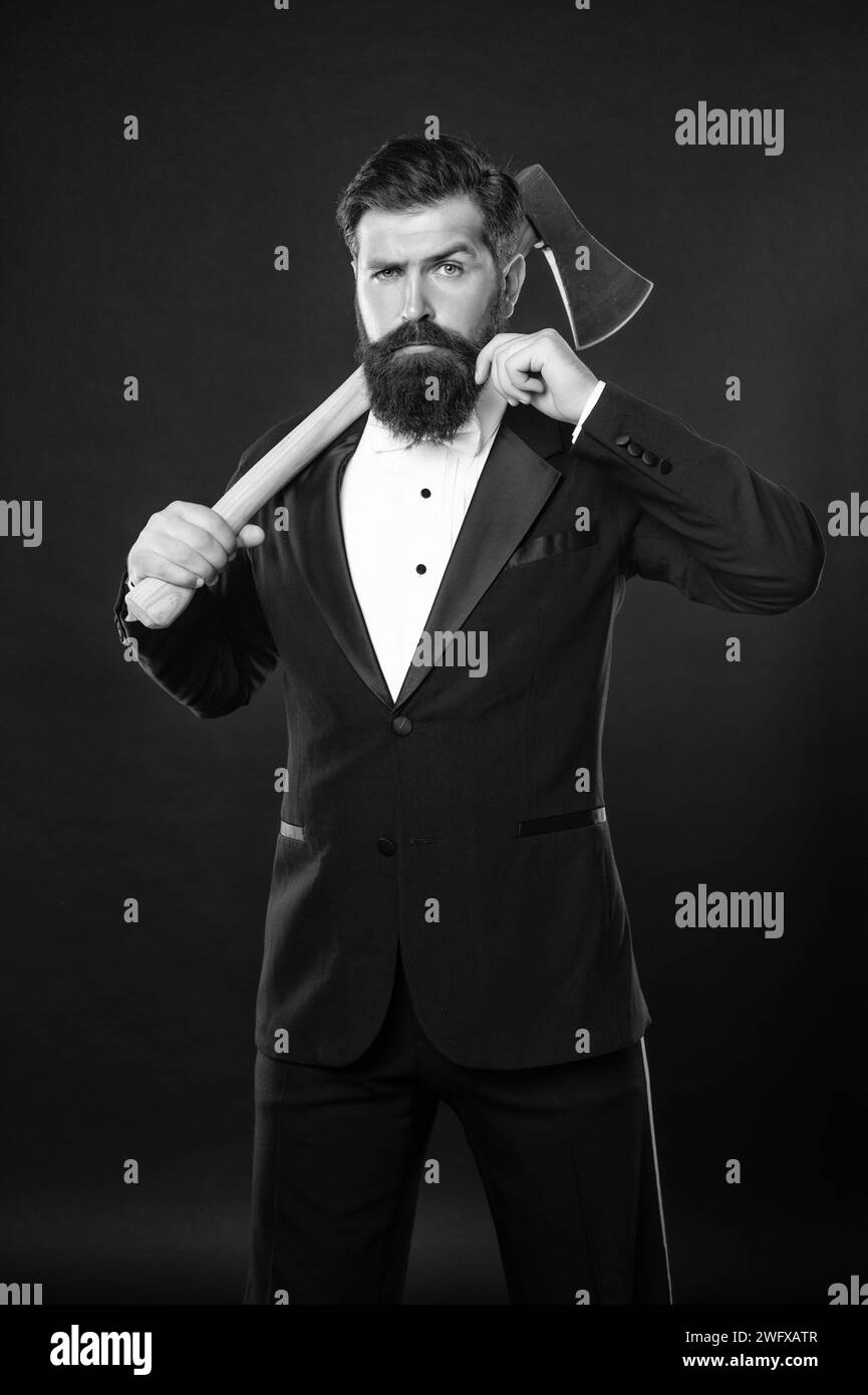Un uomo dalla barba seria che tormenta i baffi mentre trasporta ascia su sfondo scuro, barbiere. Foto Stock