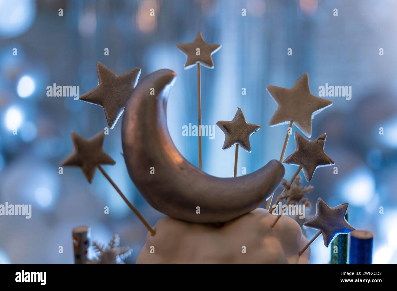 Forma a luna mezzaluna e stelle sui bastoncini. Parte della torta di compleanno. Sfondo sfocato blu e argento. Foto Stock