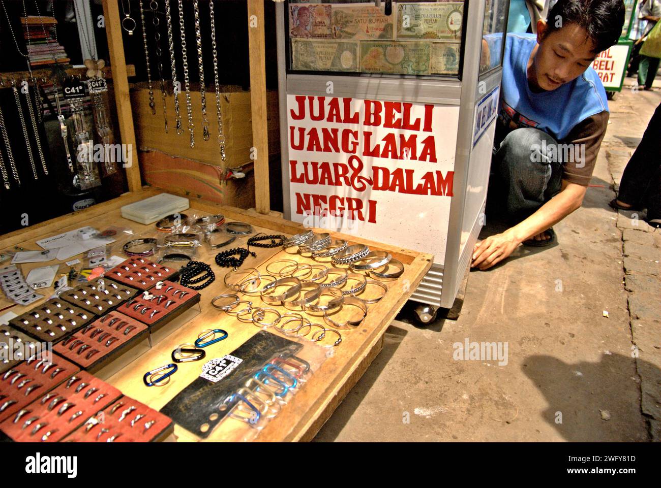 Uno shopper prepara la sua stalla di vecchie banconote indonesiane (ritirate, scadute) che vengono vendute come oggetti da collezione, situate accanto alla bancarella di gioielli in un'area di mercato stradale a Jatinegara, Giacarta Est, Indonesia. Foto Stock