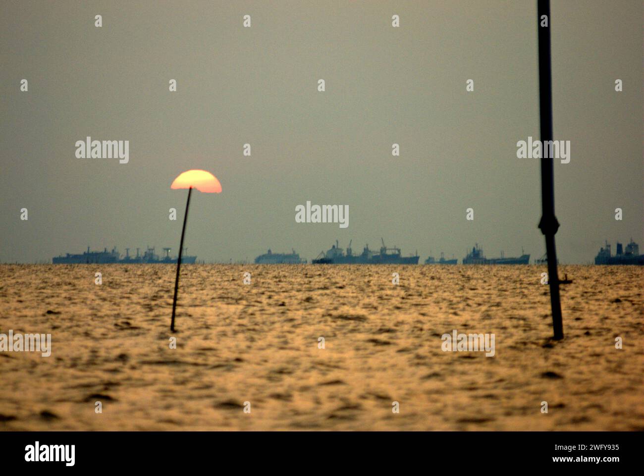 Il sole, i pali e il traffico portuale di Giacarta sulla Baia di Giacarta sono visibili dal villaggio costiero di Marunda a Giacarta, Indonesia. Foto Stock