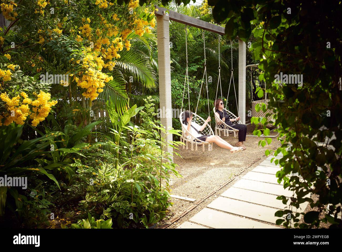 Madre e figlia che si godono la sedia a dondolo nel bellissimo e accogliente giardino nel pomeriggio Foto Stock
