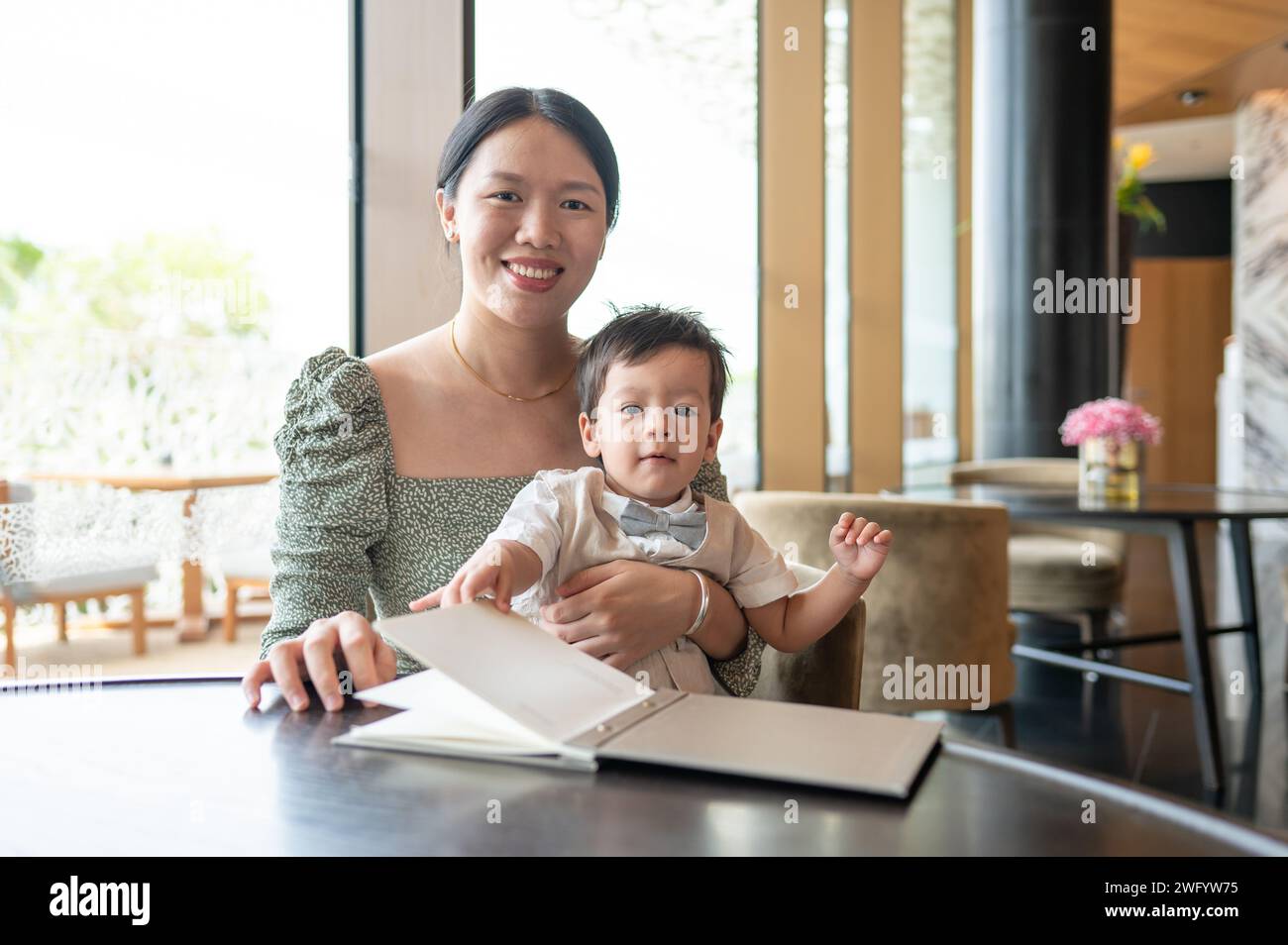 Un bambino multirazziale di un anno che festeggia il suo primo compleanno con la sua bella madre sorridente in un ristorante pronto a ordinare il cibo Foto Stock