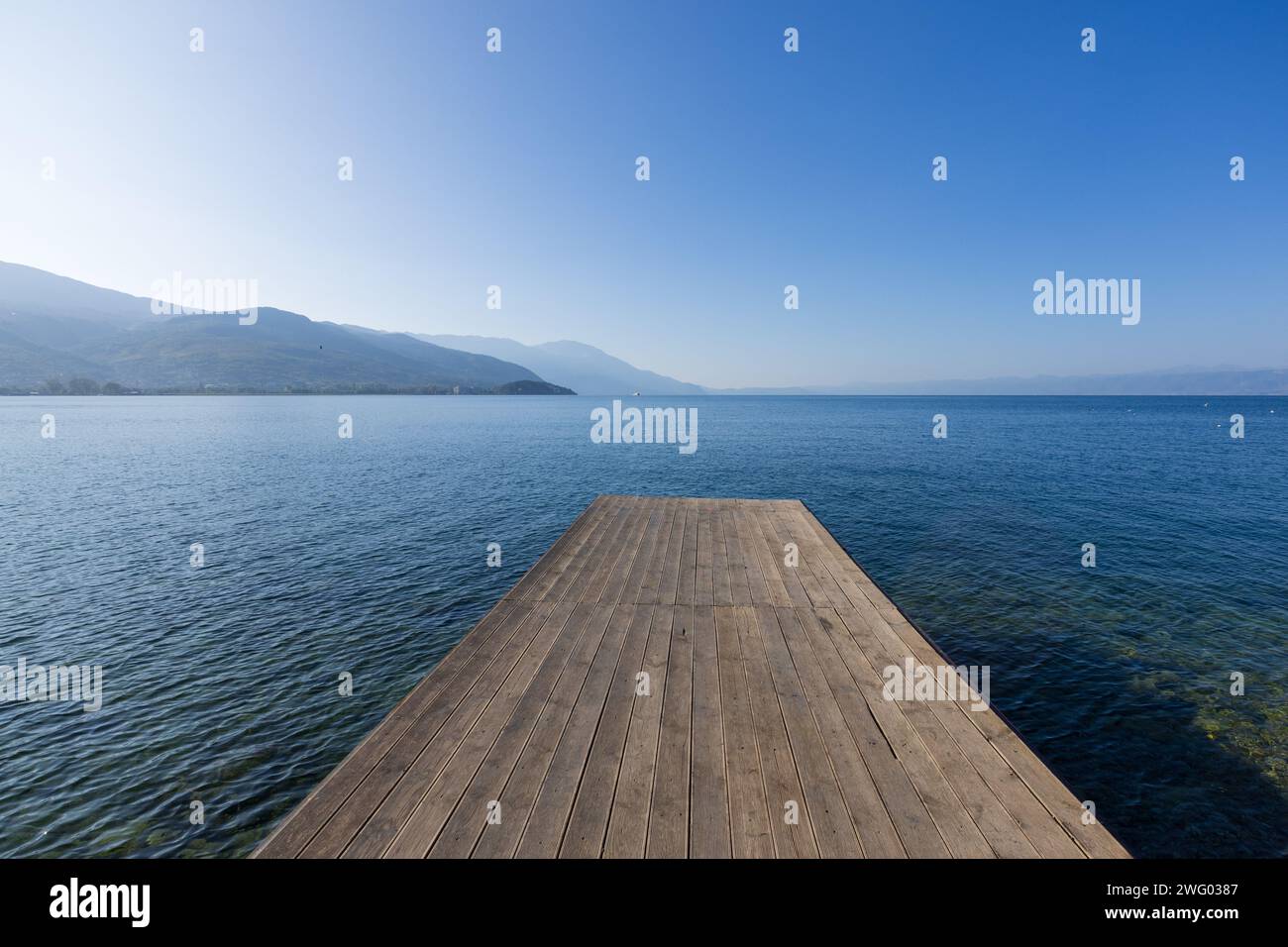 Un molo di legno sulla passerella vicino a Ohrid, sul lago di Ohrid, nella Macedonia del Nord, che si stende sulle acque blu del lago in una splendida giornata di sole. Foto Stock