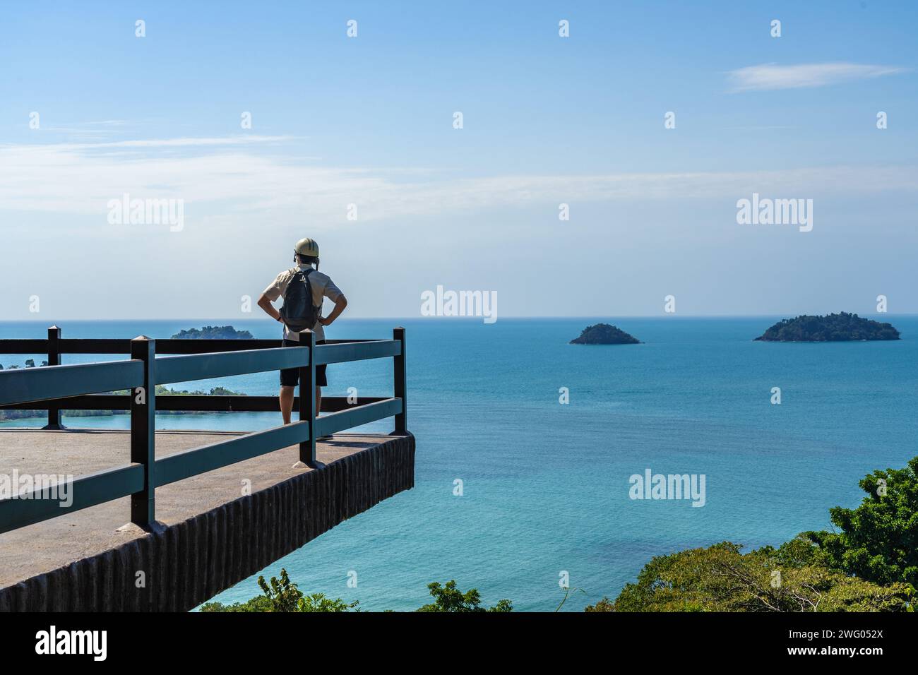 Turista maschile che indossa un piccolo zaino e un casco da motociclista in piedi e guarda la vista dell'oceano da un punto di osservazione a Koh Chang, Thailandia, a bordo di un b Foto Stock