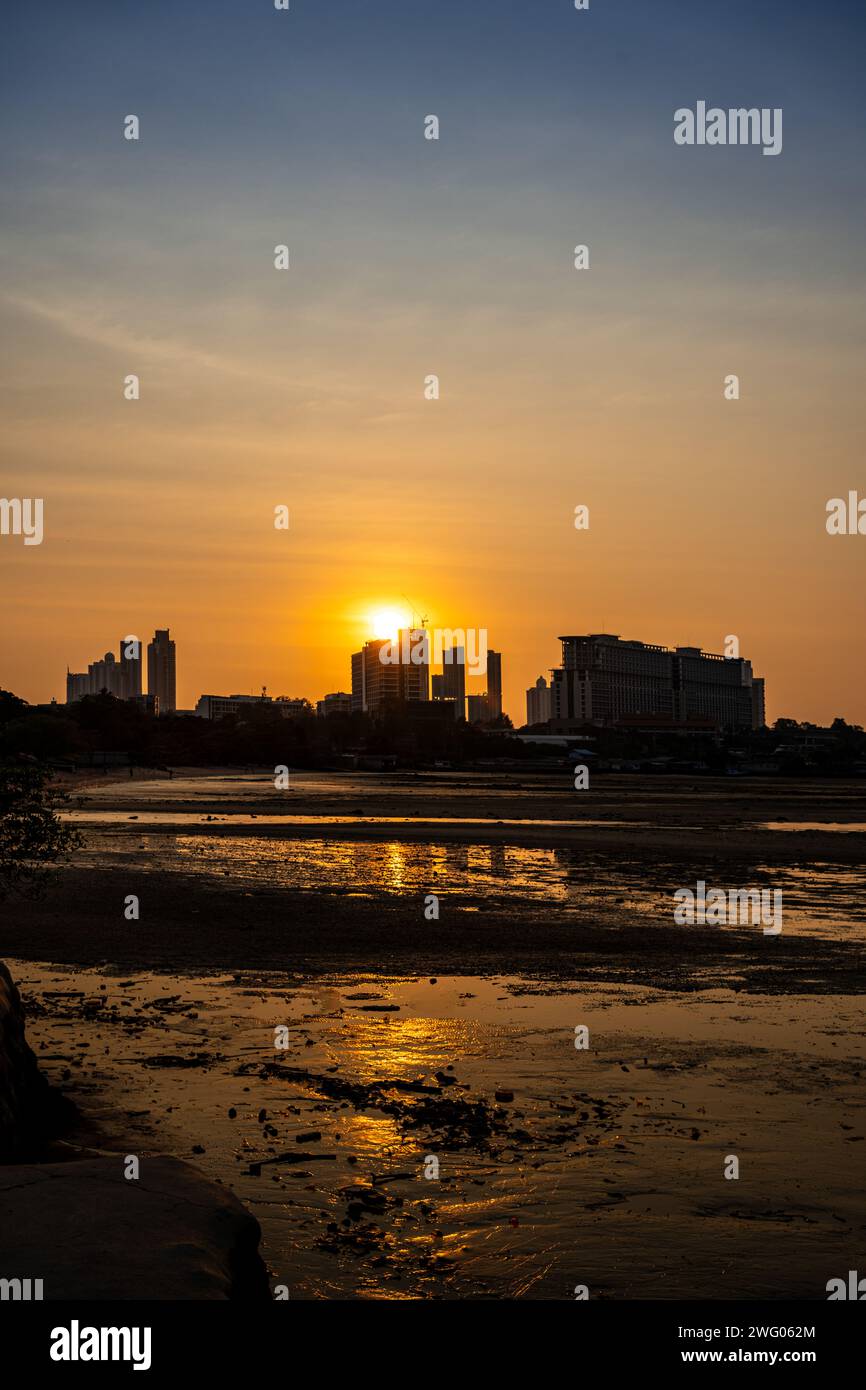 Splendida vista del tramonto serale dietro gli edifici sagomati di Pattaya, Thailandia, con il sole riflesso sull'acqua in primo piano Foto Stock