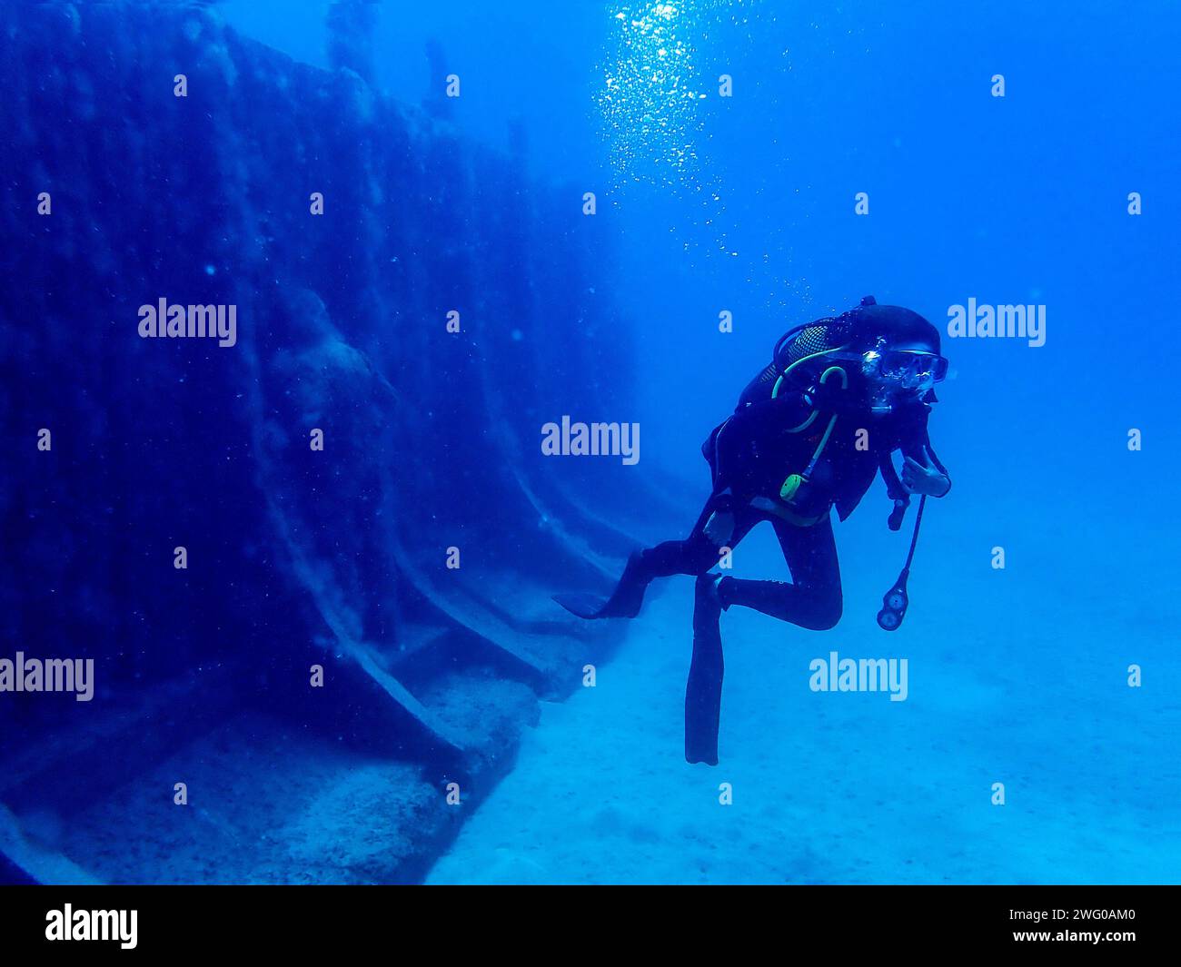 Il subacqueo si affaccia sull'abisso accanto a un muro sommerso nelle acque azzurre di Lanzarote, un'esplorazione tranquilla del blu profondo Foto Stock