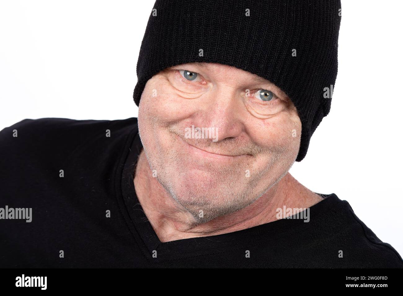 Uomo di mezza età sorridente con T-shirt e cappello neri, Ritratto sicuro su sfondo bianco - stile di vita e moda casual per adulti maturi Foto Stock
