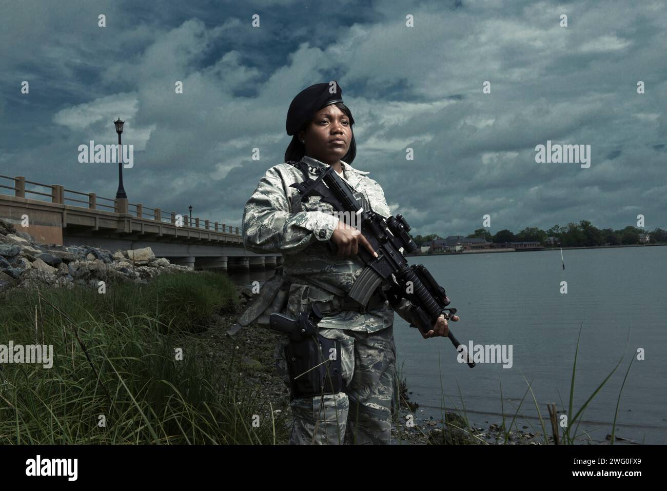 Un afroamericano, donna, Airman delle forze di sicurezza dell'Air Force in uniforme posa con il suo fucile M-4 vicino alla costa di un fiume. Foto Stock