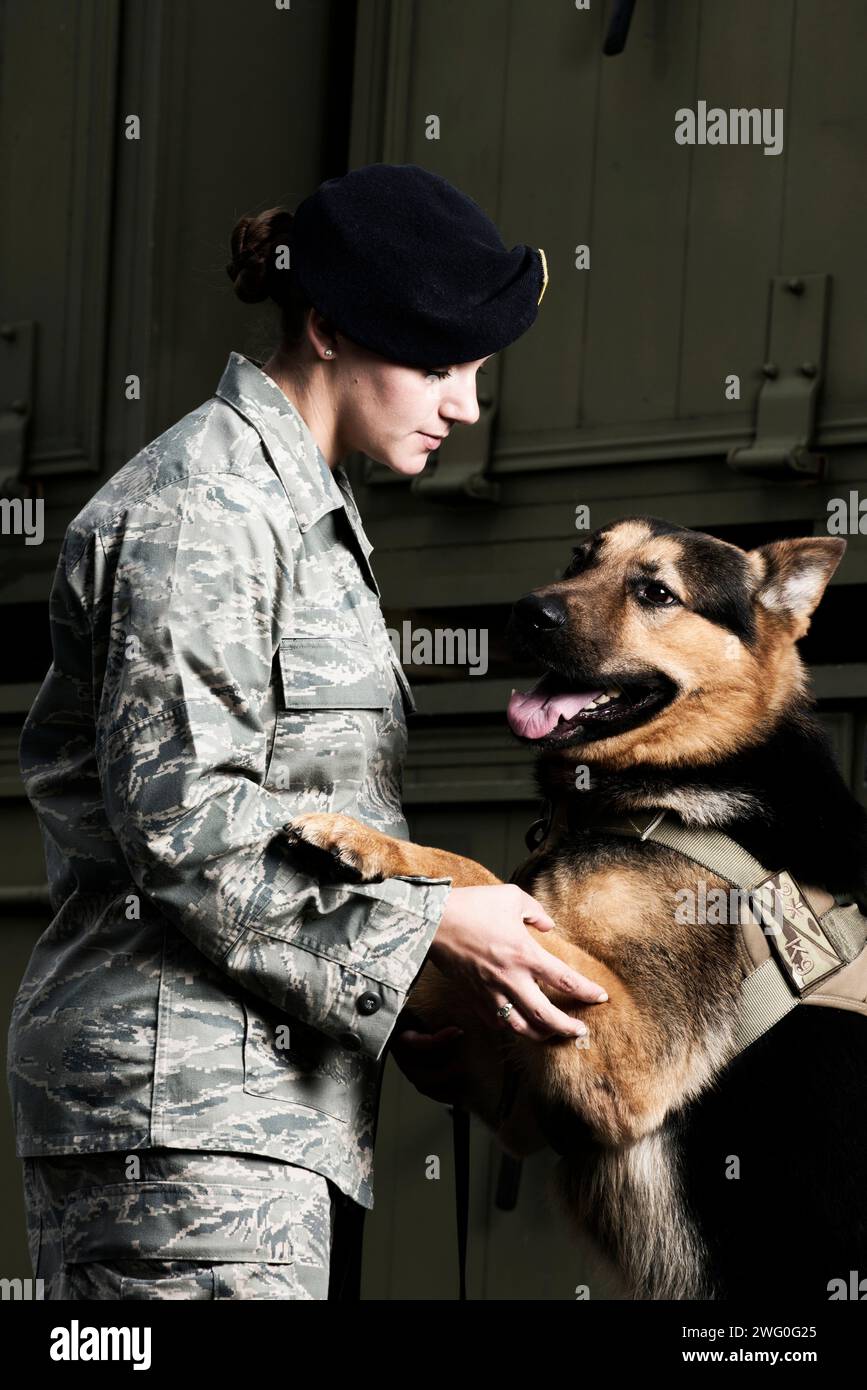 Una donna caucasica Airman delle forze di sicurezza dell'aeronautica militare in uniforme dà al suo cane da lavoro militare il comando di saltare in alto. Foto Stock