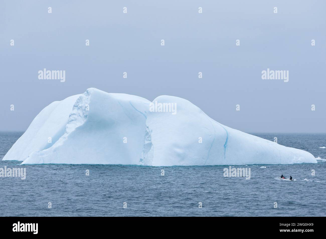 Un piccolo peschereccio passa davanti a un iceberg sulla costa orientale della Groenlandia vicino alla città di Ammassalik. Foto Stock
