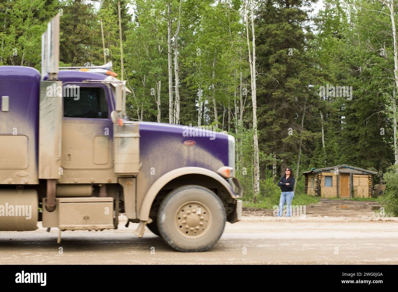Una donna guarda mentre un semi viaggia su una strada sterrata in Alberta, Canada. Foto Stock