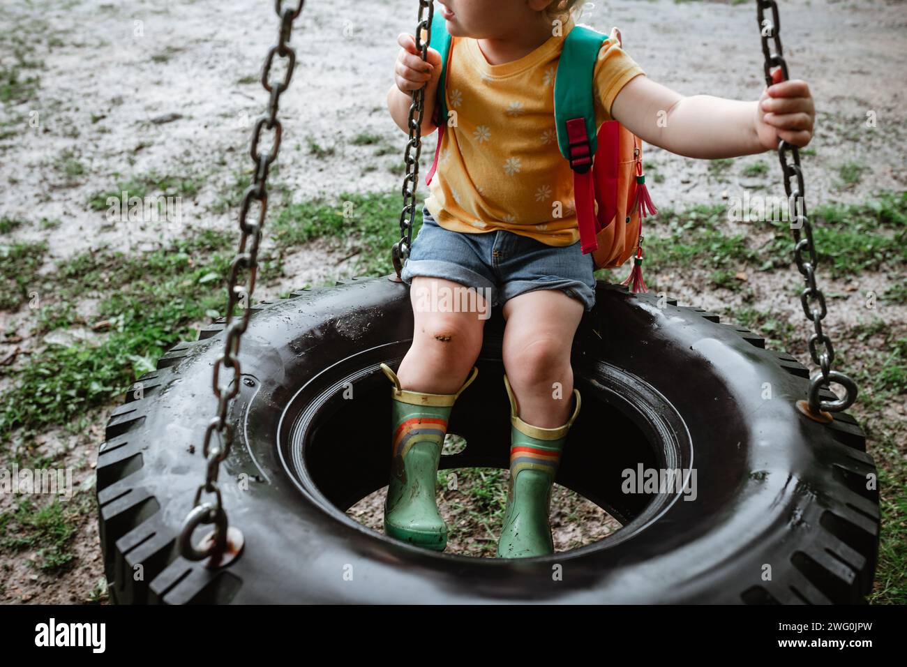 Bambino vestito coloratamente seduto sulla ruota girevole nelle giornate di pioggia Foto Stock